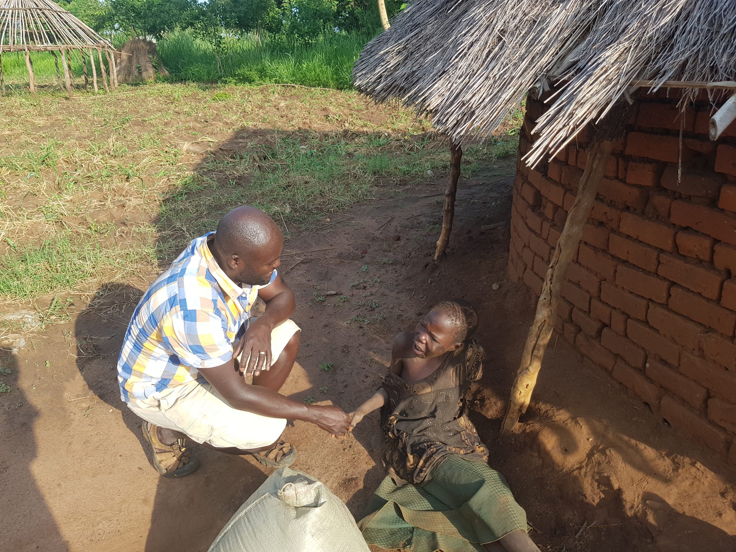 Acholi Resilience field worker attending to a child at home during a village malaria outreach visit